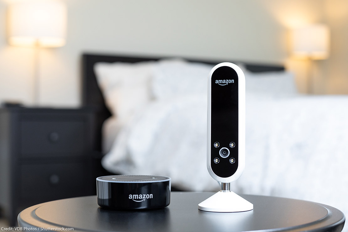 Amazon camera and Amazon Alexa speaker next to each other on a bedside table.