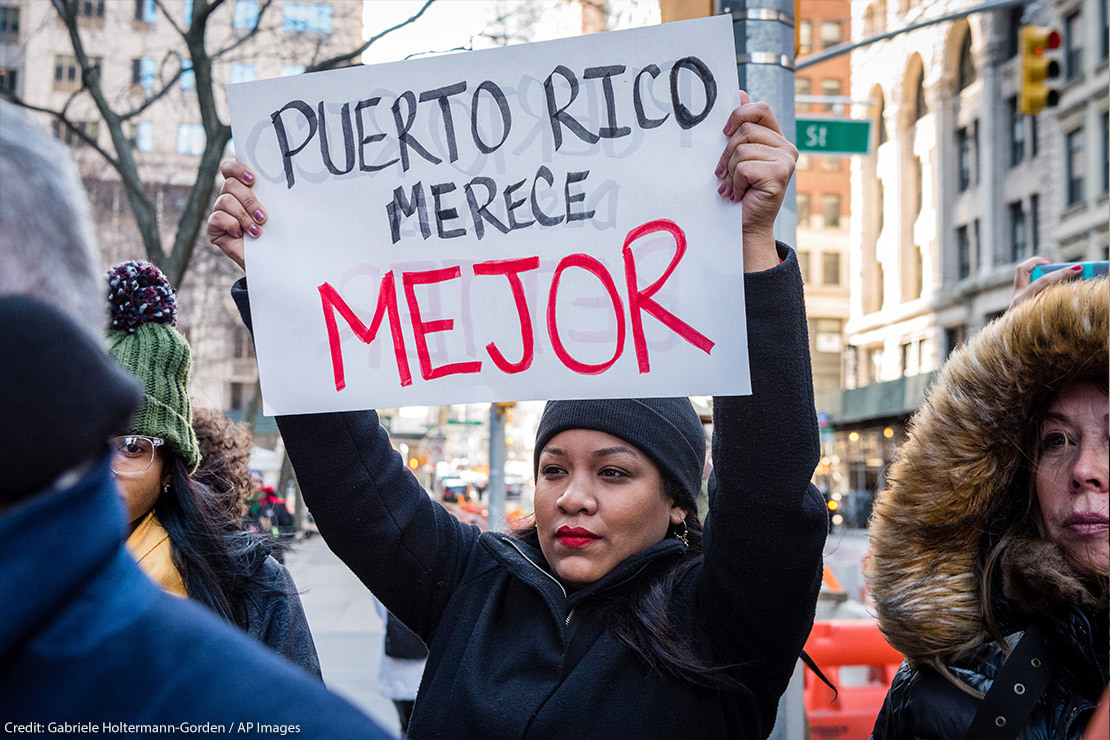 Protestor holds sign that reads "Puerto Rico deserves better" in Spanish