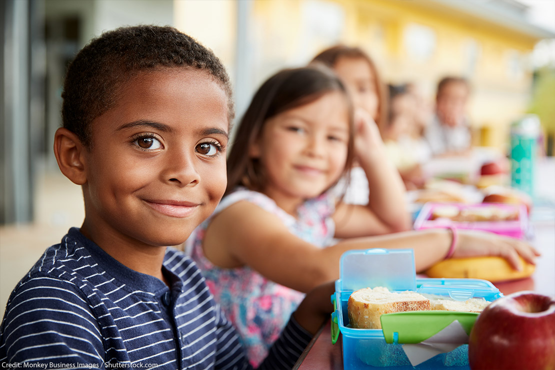 Young boy and girl sitting at a lunch table smiling at camera.