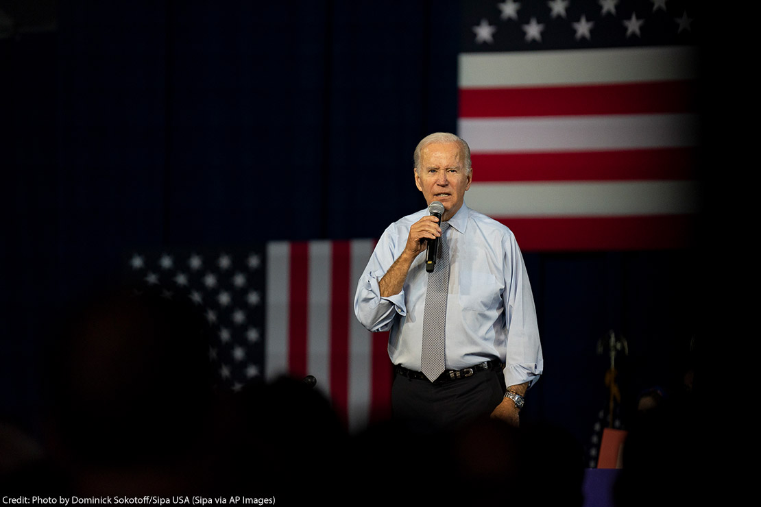 Joe Biden speaking in front of several American flags.