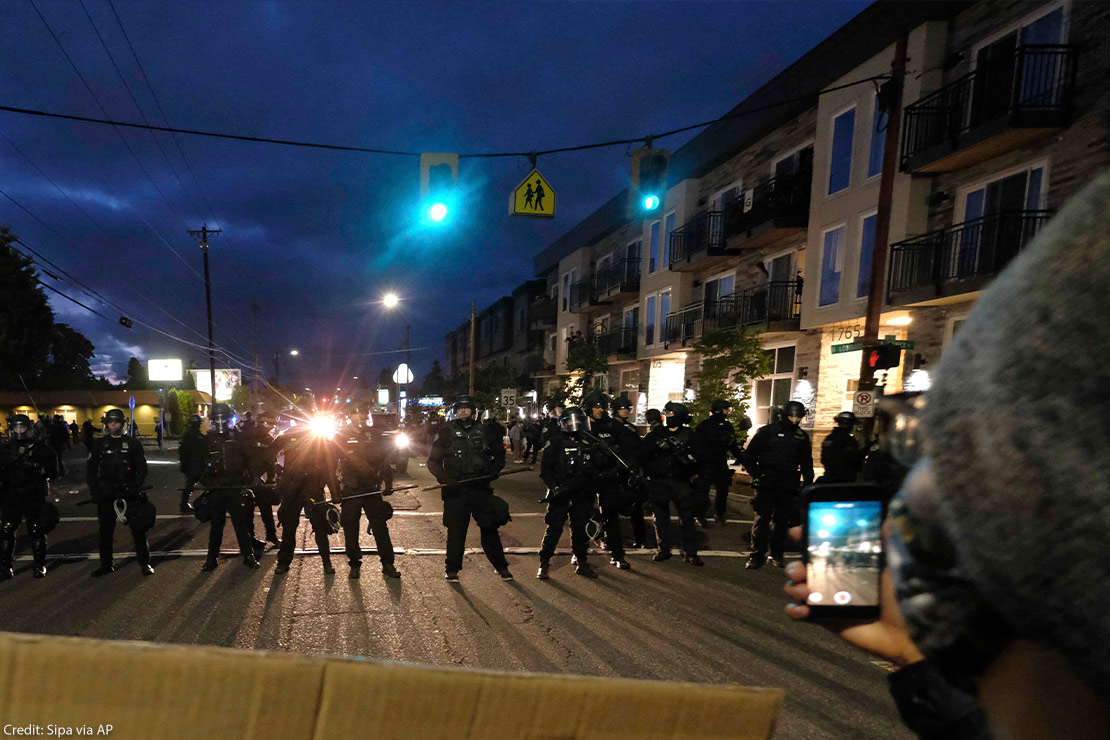 A protester records police in riot gear as they form a wall to push crowds of demonstrators in Portland, Ore., on June 30, 2020, in the wake the murder of George Floyd.