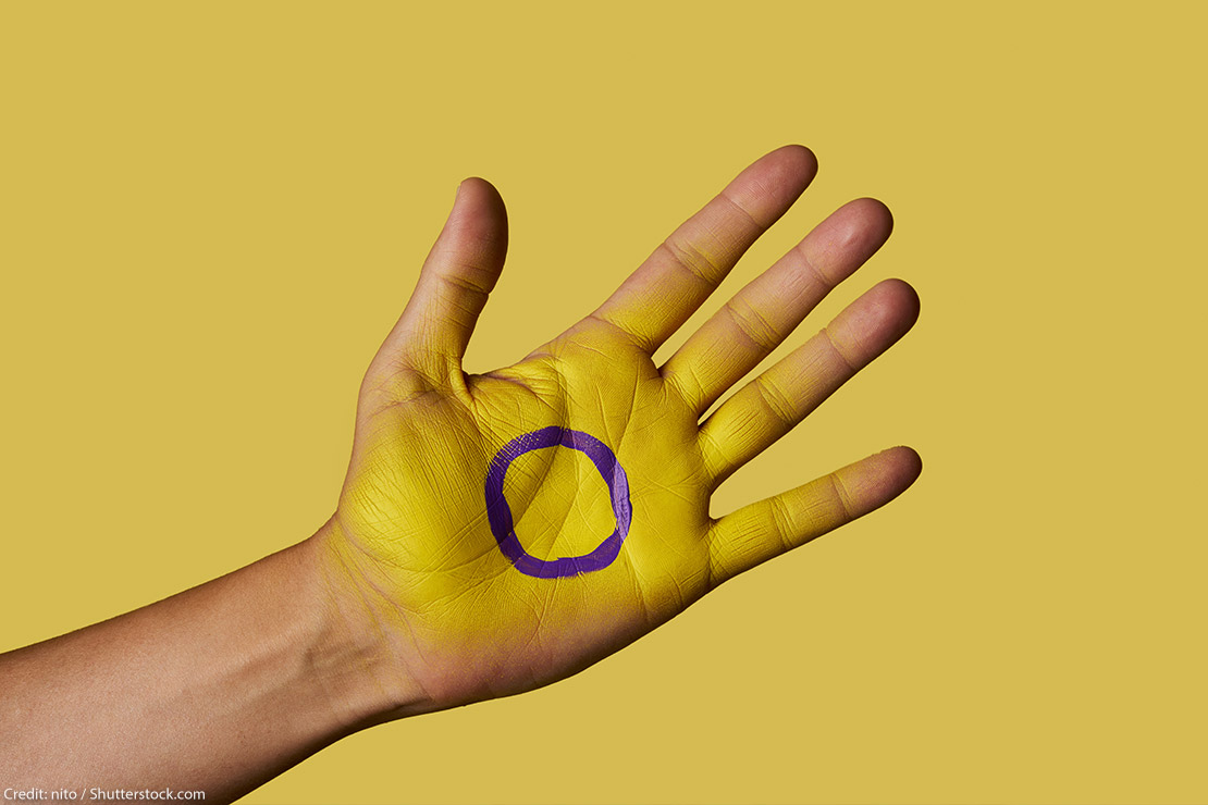 A closeup of the intersex flag painted on the palm of a person's hand.