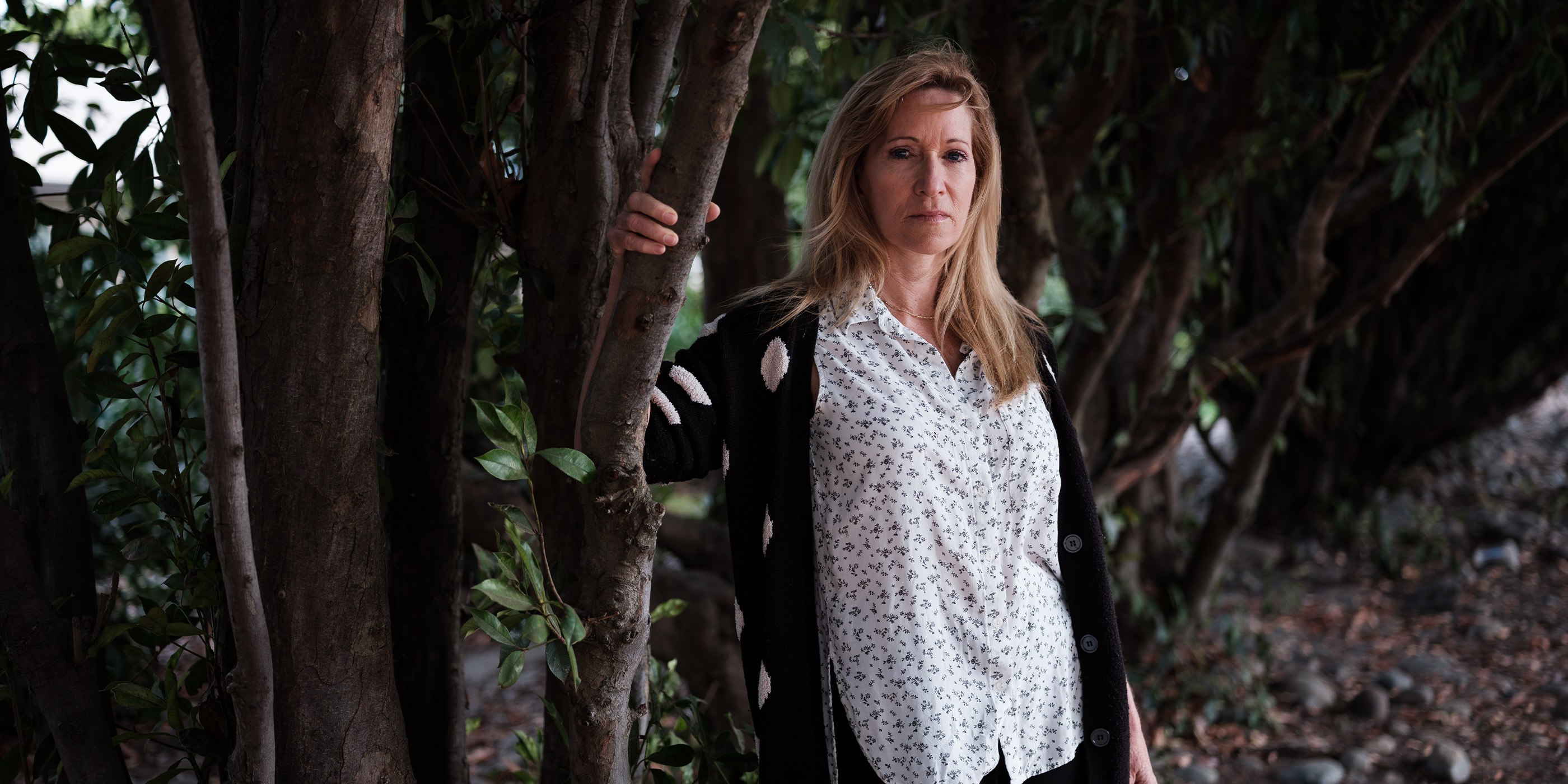 Kristen DiAngelo, sex worker and activist, in white shirt standing with arm on a tree branch