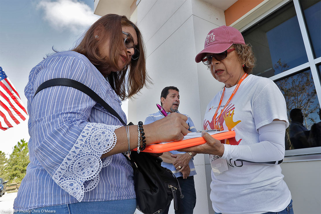 Canvasser Ana M. Vigo, right, registers a woman, left, to vote as a male bystander looks on outside the Polk County Tax Collectors office in Davenport, Fla.