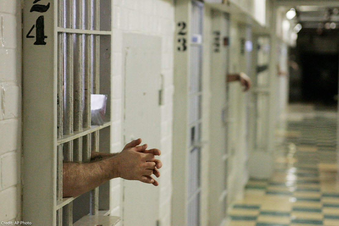 Prisoners reach through the metal bars of their cells.