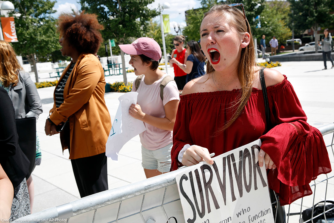 A recent graduate shouts and holds sign that reads "survivor" as Betsey Devos speaks on college campus about changes to Title IX