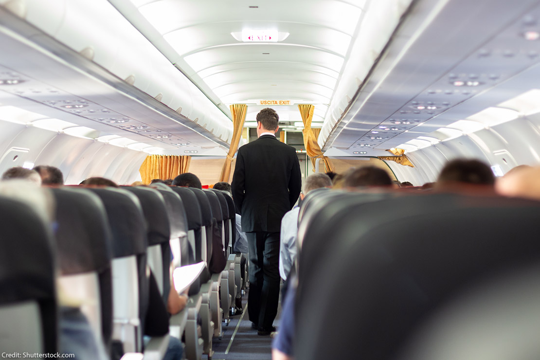 A flight attendant wearing a suit walking through the aisle of a plane.