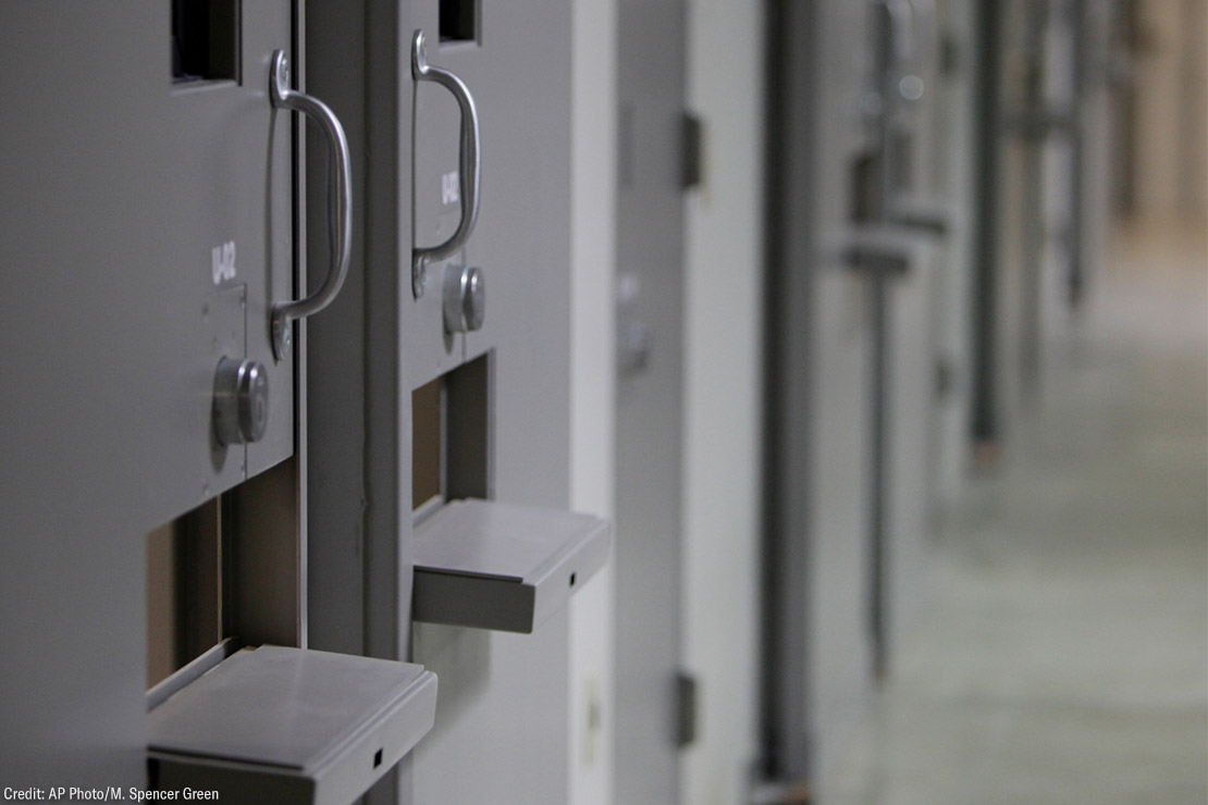 A hallway in a detention center with a line of closed cell doors.