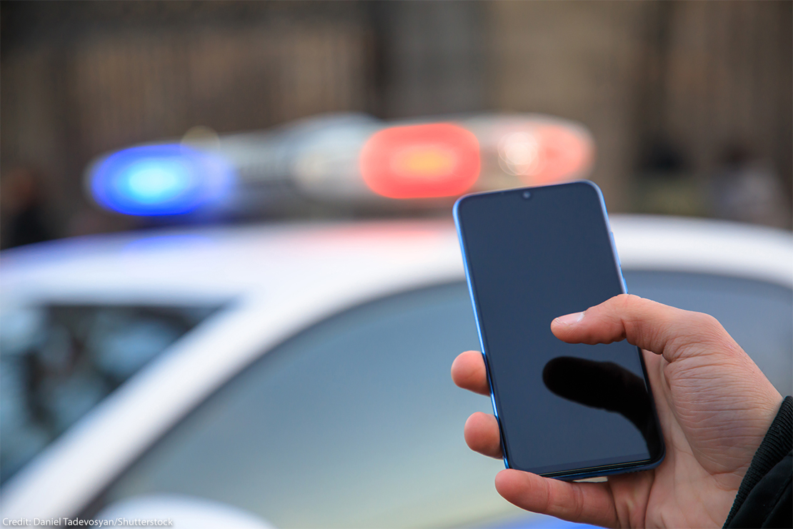 Hand holding phone with police car lights shining in the background.