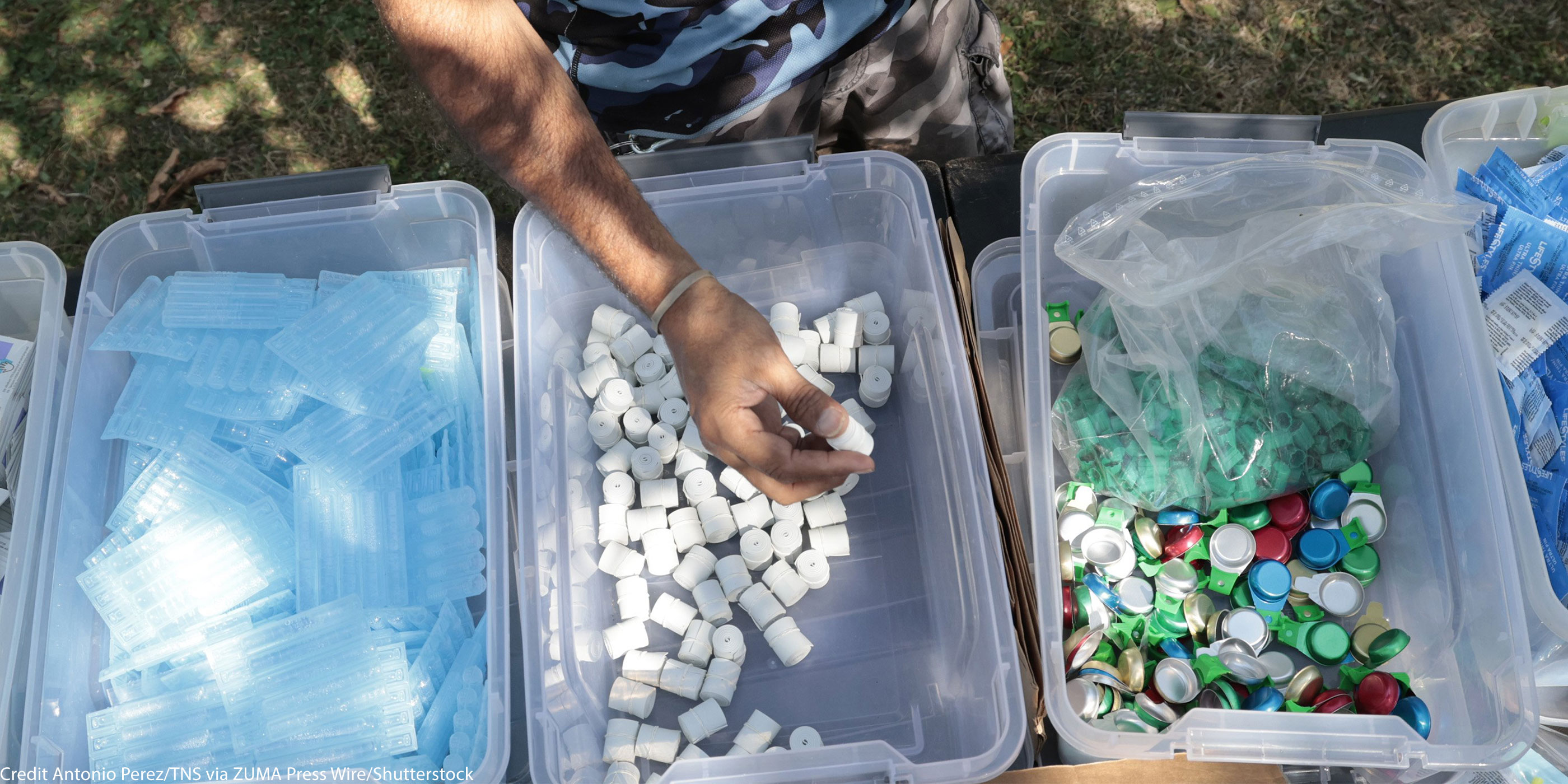 A hand taking harm reduction supplies for addicts from the middle of 3 bins.