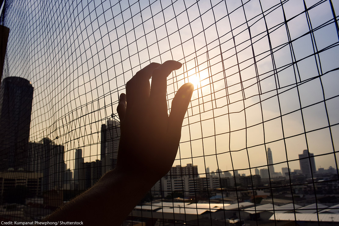 The silhouette of a hand holding on to a gate.