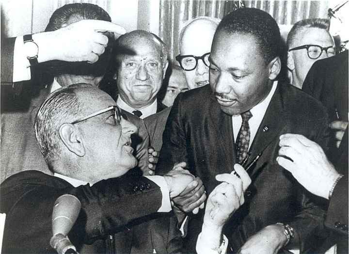 President Lyndon Johnson shakes the hand of Dr. Martin Luther King Jr., as he hands him a pen at the signing of the Civil Rights Act of 1964 on Thursday, July 2, 1964 at The White House.