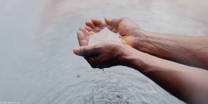 Two hands holding water, creating ripples on the surface below.