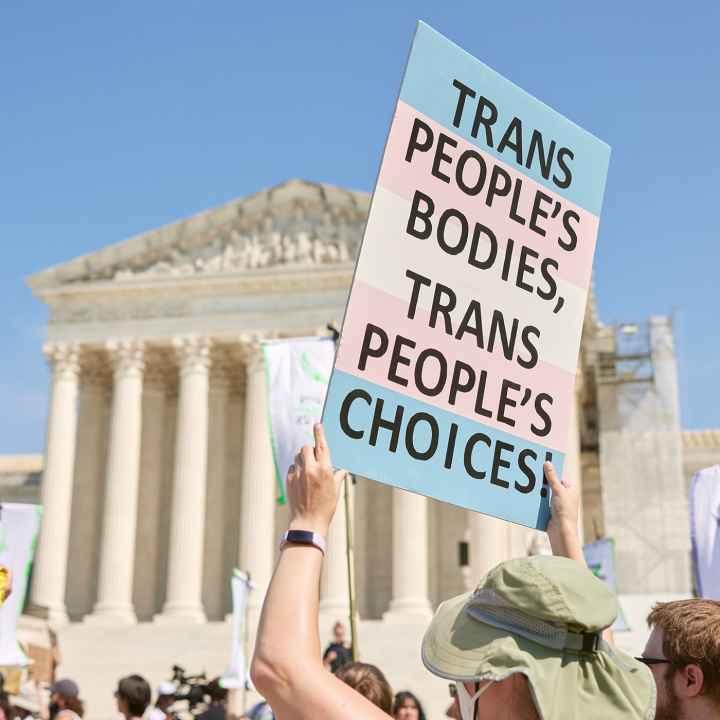 A demonstrator at a march in front of the Supreme Court holds up a sign reading "TRANS PEOPLE'S BODIES, TRANS PEOPLE'S CHOICES".