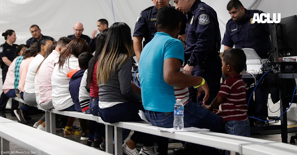 Migrants seated in a processing area at a tent courtroom