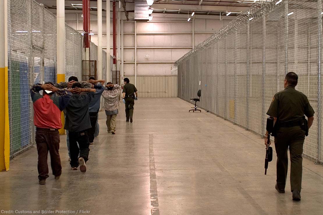 Armed CBP guard watches inmates in a CBP facility